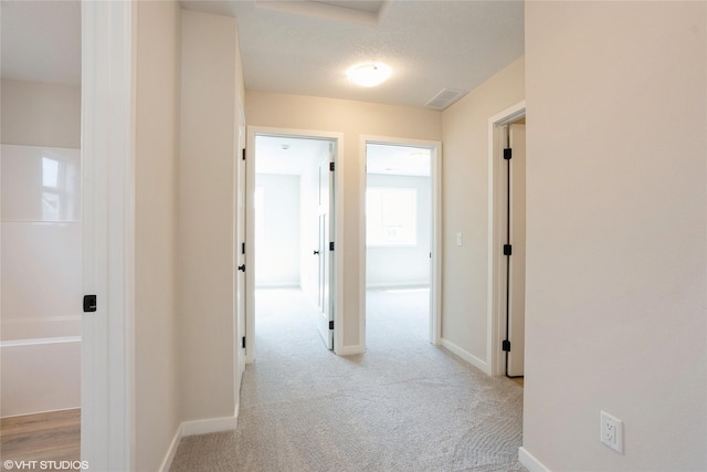 hallway featuring light carpet, visible vents, and baseboards