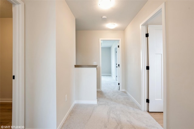 hallway featuring baseboards and light colored carpet
