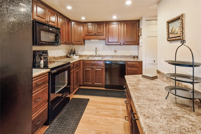 kitchen with black appliances, light hardwood / wood-style flooring, light stone countertops, and sink