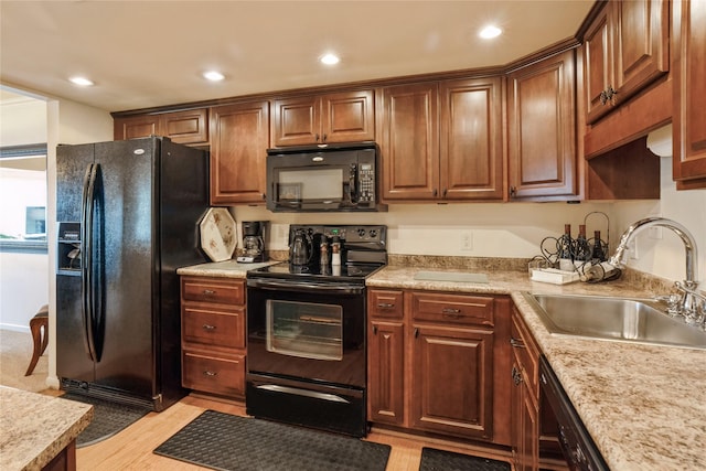 kitchen featuring black appliances, light stone countertops, light hardwood / wood-style floors, and sink