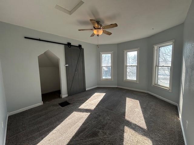 carpeted empty room with ceiling fan and a barn door