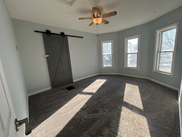 spare room with ceiling fan, a barn door, a healthy amount of sunlight, and dark colored carpet