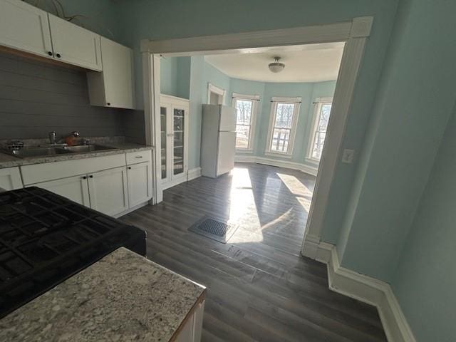 kitchen featuring dark hardwood / wood-style floors, white refrigerator, white cabinets, light stone counters, and sink