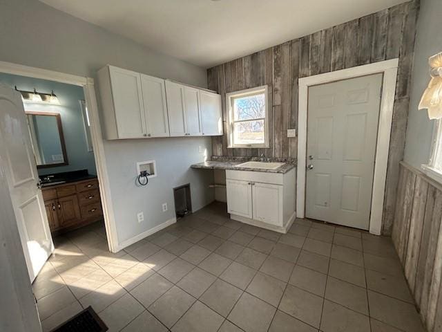 kitchen featuring white cabinets, light tile patterned floors, sink, and wood walls