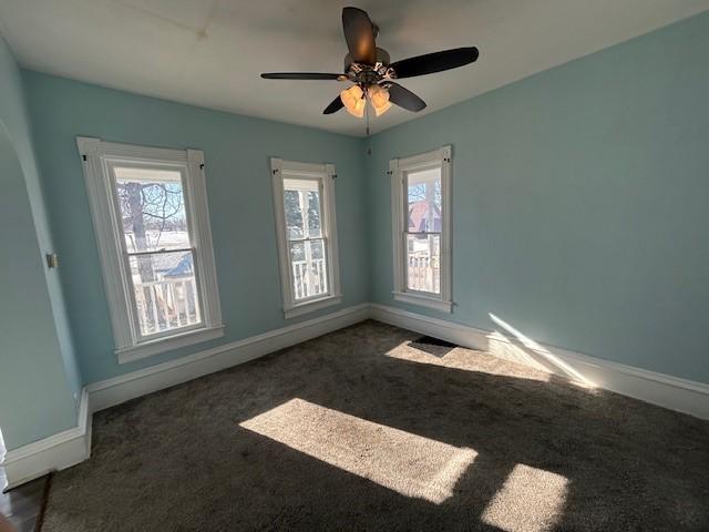 empty room with ceiling fan, a healthy amount of sunlight, and dark colored carpet