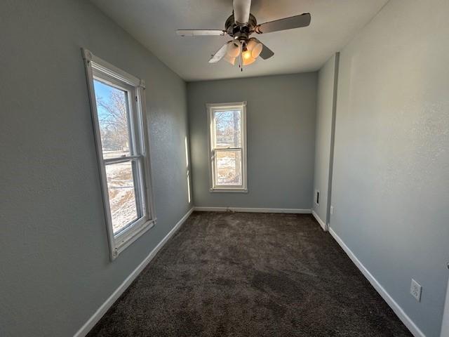 unfurnished room featuring ceiling fan, plenty of natural light, and dark colored carpet