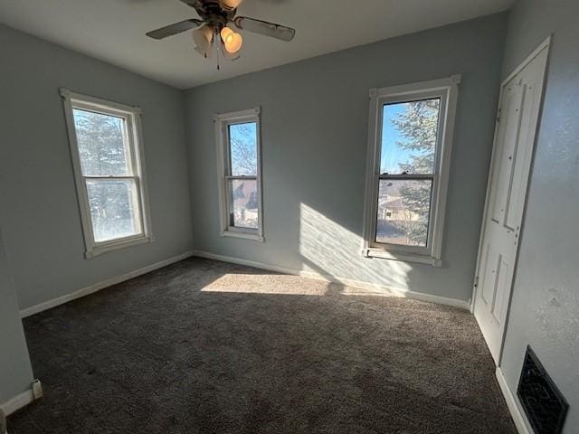 spare room with ceiling fan, dark carpet, and a wealth of natural light