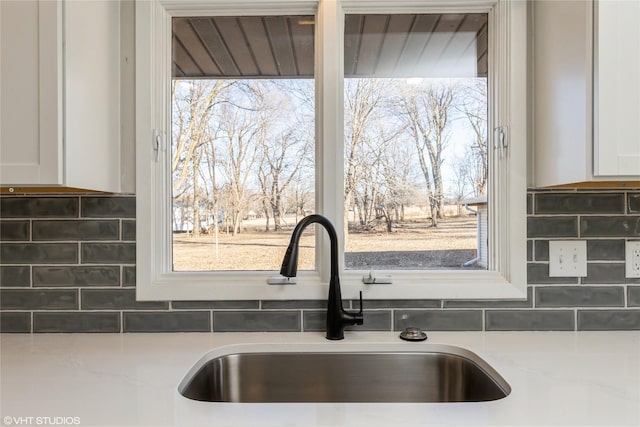 details featuring light stone countertops, a sink, white cabinets, and decorative backsplash