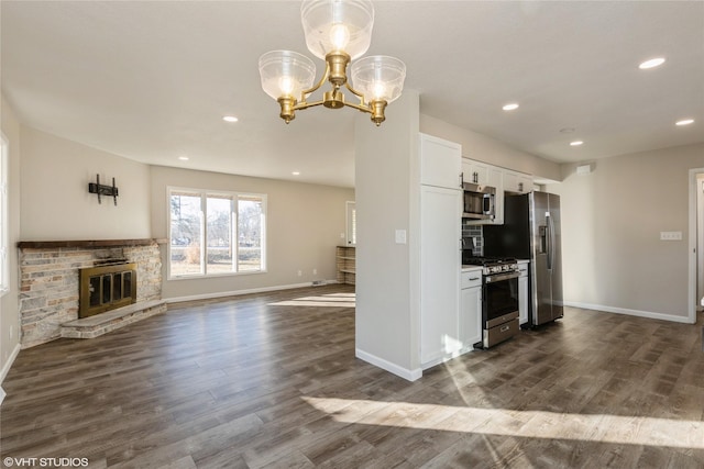 kitchen featuring a stone fireplace, an inviting chandelier, dark hardwood / wood-style floors, stainless steel appliances, and white cabinets