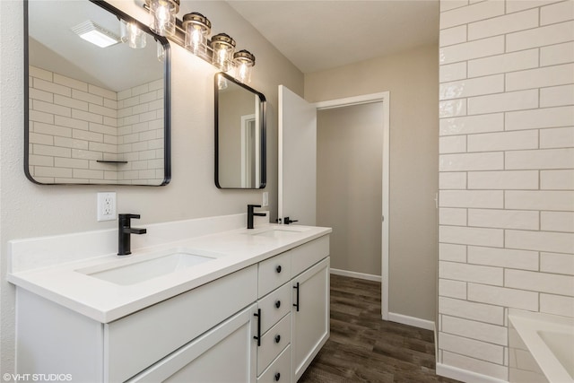 bathroom featuring a bathtub, double vanity, a sink, and wood finished floors