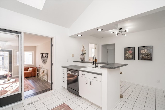 kitchen with black dishwasher, white cabinetry, sink, lofted ceiling with skylight, and kitchen peninsula