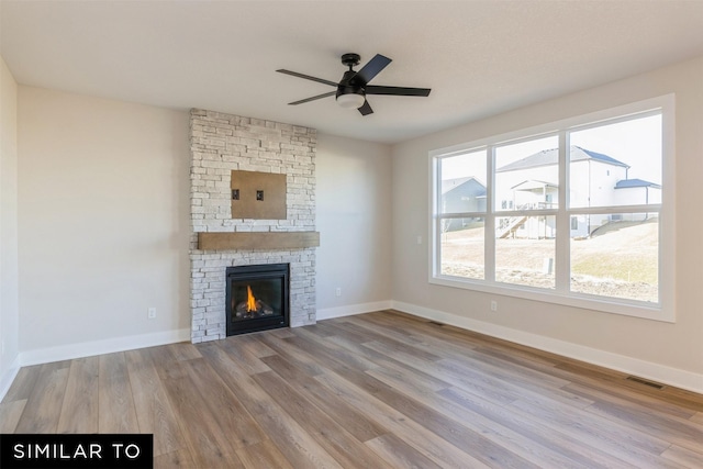 unfurnished living room with ceiling fan, a stone fireplace, and light hardwood / wood-style floors