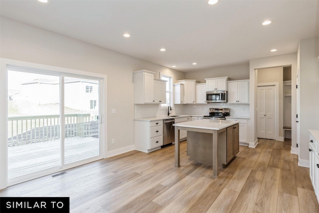 kitchen with white cabinets, a kitchen island, sink, light hardwood / wood-style flooring, and stainless steel appliances