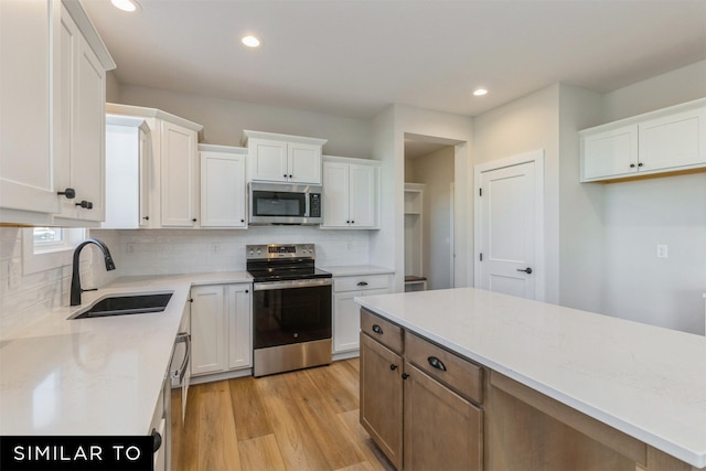 kitchen with white cabinets, appliances with stainless steel finishes, decorative backsplash, sink, and light hardwood / wood-style flooring