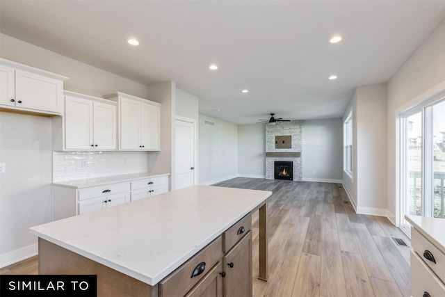 kitchen with a center island, backsplash, white cabinetry, and light stone counters