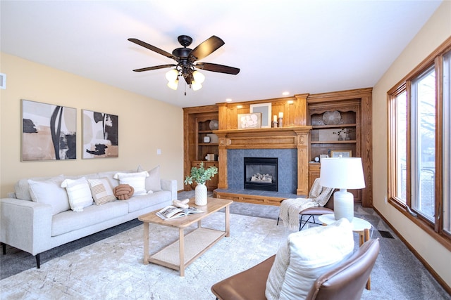 living area featuring baseboards, visible vents, built in features, a glass covered fireplace, and ceiling fan