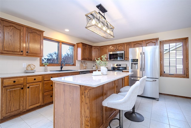 kitchen with brown cabinetry, stainless steel appliances, a sink, and a center island