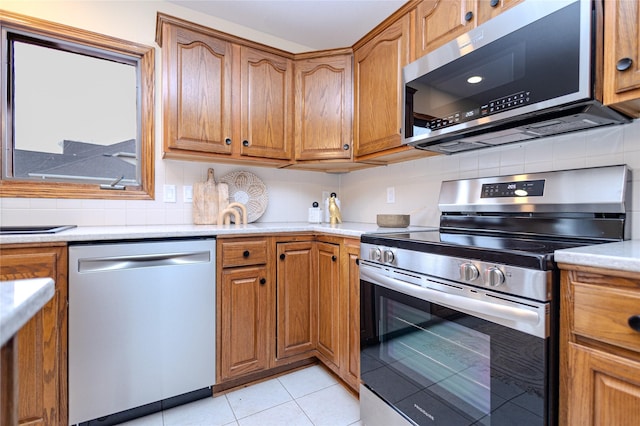 kitchen with light tile patterned floors, light countertops, appliances with stainless steel finishes, backsplash, and brown cabinetry