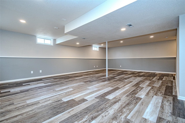 below grade area with baseboards, a textured ceiling, visible vents, and wood finished floors