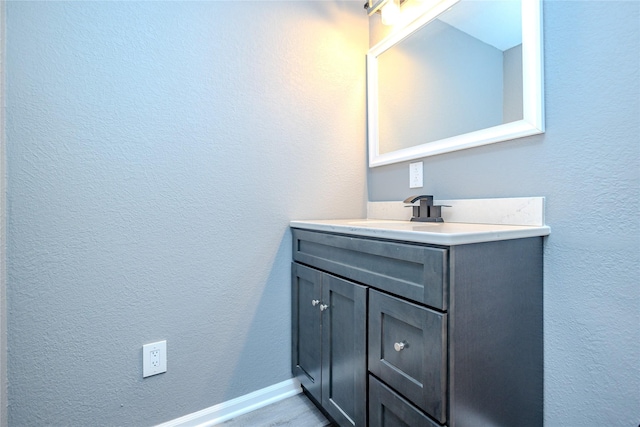 bathroom featuring a textured wall, baseboards, wood finished floors, and vanity