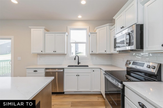 kitchen featuring appliances with stainless steel finishes, white cabinetry, decorative backsplash, sink, and light stone counters