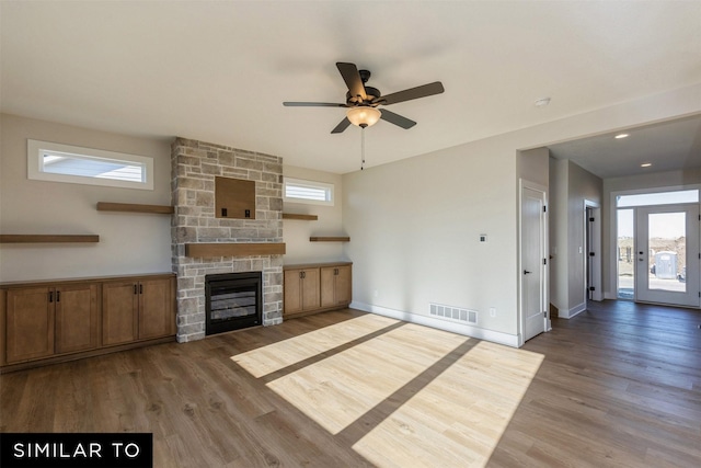 unfurnished living room with ceiling fan, dark hardwood / wood-style flooring, and a stone fireplace