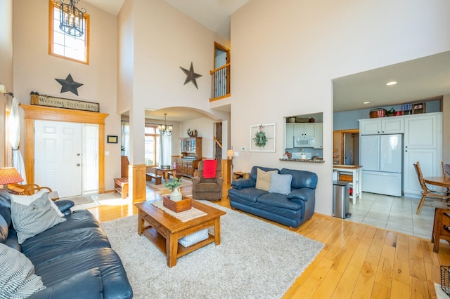 living room with an inviting chandelier, a towering ceiling, and light wood-type flooring