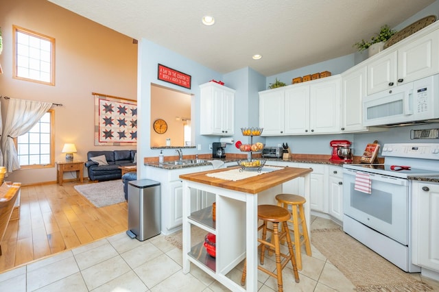 kitchen featuring white cabinets, white appliances, light tile patterned floors, and butcher block counters