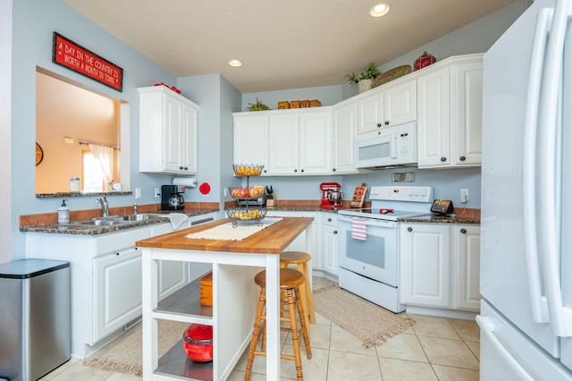 kitchen with white appliances, a kitchen bar, light tile patterned floors, white cabinets, and sink