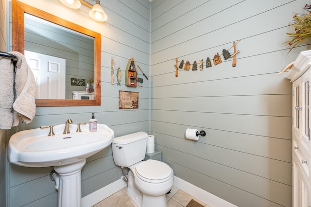 bathroom with sink, toilet, wood walls, and tile patterned flooring