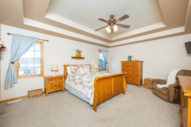 bedroom featuring ceiling fan, a tray ceiling, and light carpet