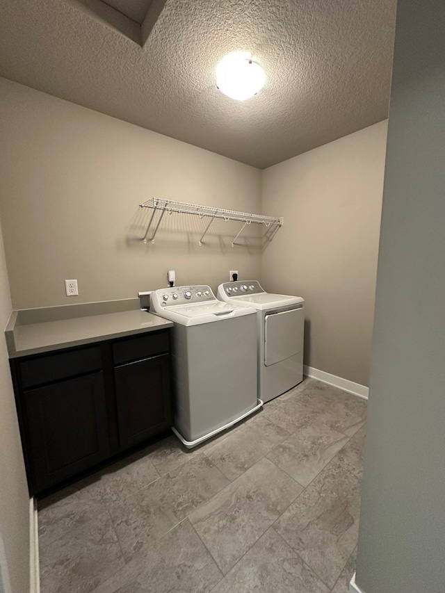 laundry area with cabinets, a textured ceiling, and washer and clothes dryer