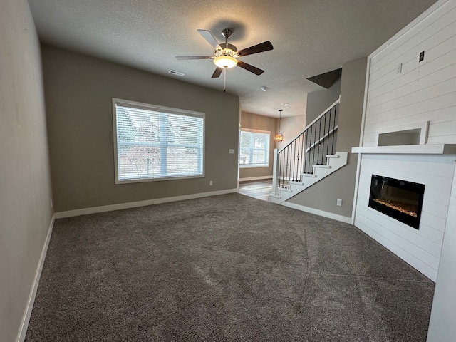 unfurnished living room with ceiling fan, carpet, a fireplace, and a textured ceiling