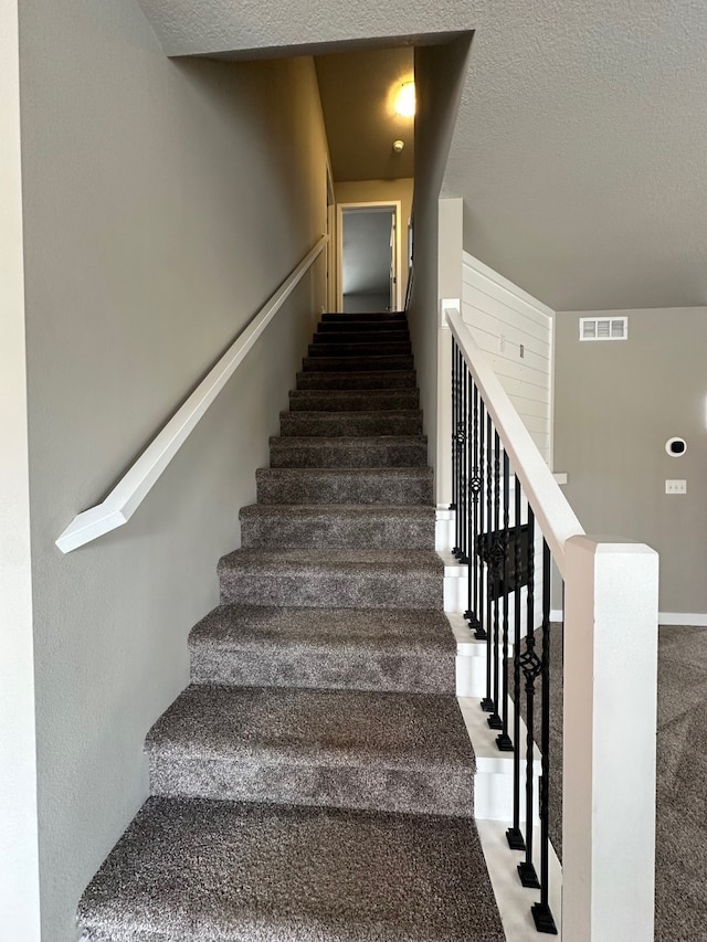 staircase with a textured ceiling and carpet floors