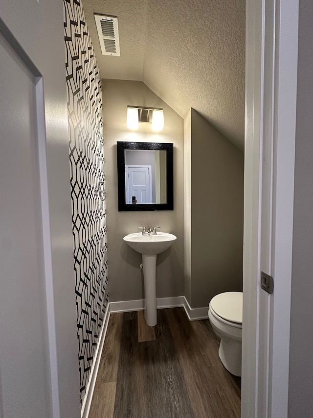 bathroom with a textured ceiling, wood-type flooring, sink, toilet, and vaulted ceiling