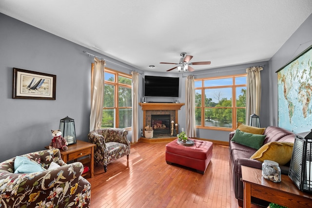 living room featuring light hardwood / wood-style floors, plenty of natural light, ceiling fan, and a tiled fireplace