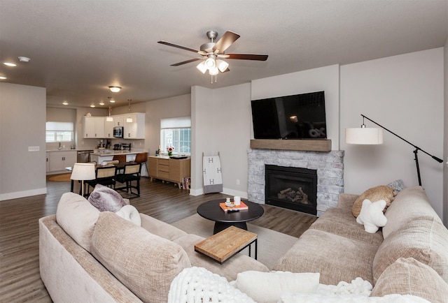 living room with ceiling fan, a stone fireplace, dark hardwood / wood-style floors, and sink