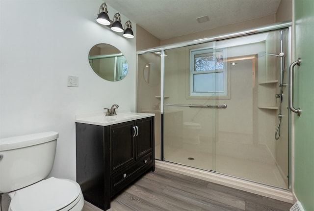 bathroom featuring wood-type flooring, a shower with door, toilet, and vanity