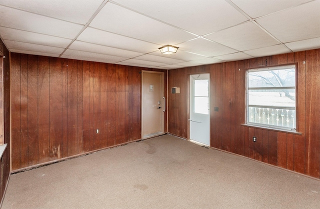 empty room with light carpet, wood walls, and a paneled ceiling