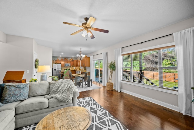 living room with ceiling fan with notable chandelier, dark wood-type flooring, and a textured ceiling