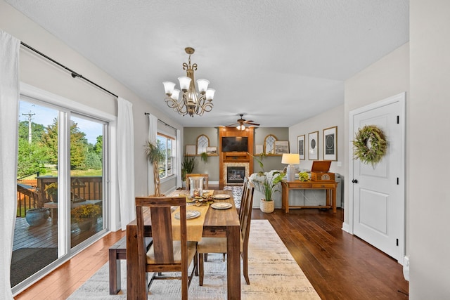 dining area featuring ceiling fan with notable chandelier, a textured ceiling, dark hardwood / wood-style flooring, and a fireplace