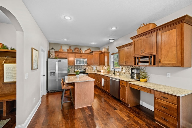 kitchen featuring light stone counters, appliances with stainless steel finishes, a center island, and a kitchen bar