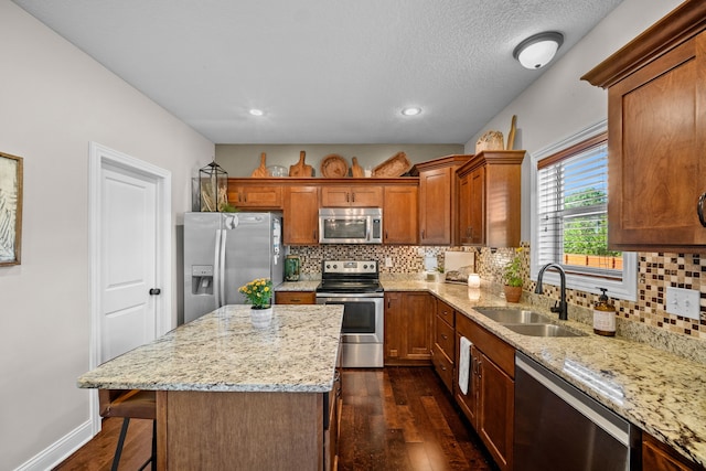 kitchen with sink, light stone counters, a center island, dark hardwood / wood-style floors, and stainless steel appliances