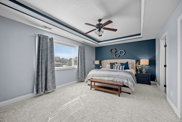 bedroom featuring ceiling fan, light colored carpet, a textured ceiling, and a tray ceiling