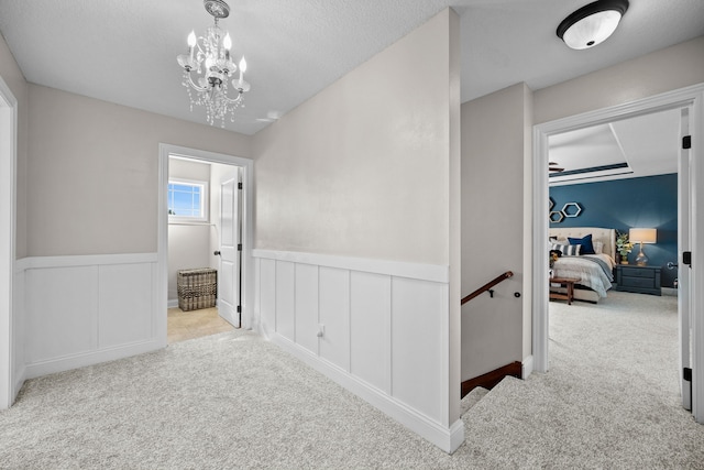 hallway with light colored carpet, a textured ceiling, and a chandelier