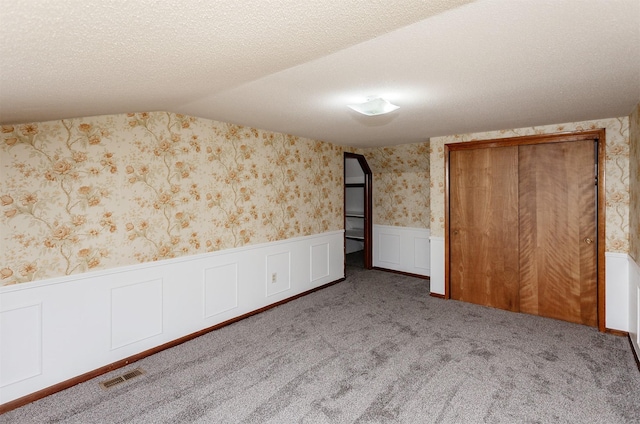 unfurnished bedroom with light colored carpet, a textured ceiling, and vaulted ceiling