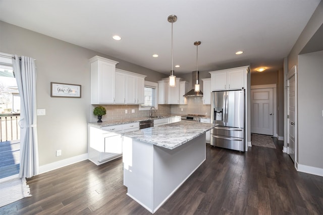 kitchen featuring appliances with stainless steel finishes, decorative light fixtures, white cabinetry, a center island, and wall chimney range hood