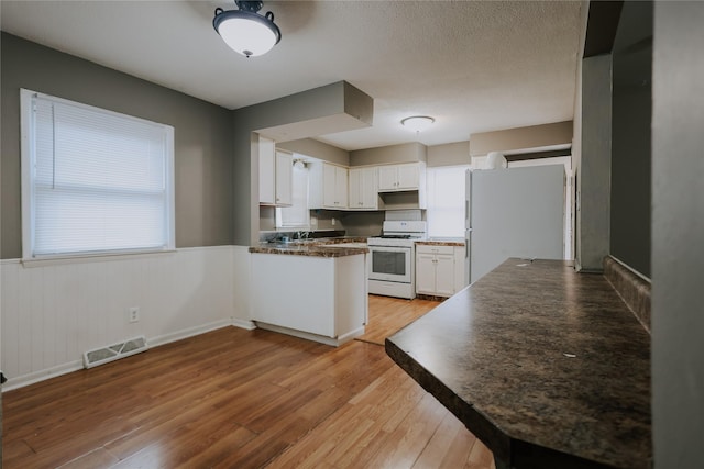 kitchen with kitchen peninsula, white appliances, white cabinets, and light hardwood / wood-style floors