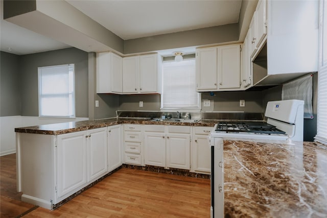 kitchen featuring white cabinets, kitchen peninsula, white gas range, and sink