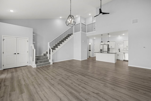 unfurnished living room with a towering ceiling, ceiling fan with notable chandelier, and hardwood / wood-style flooring